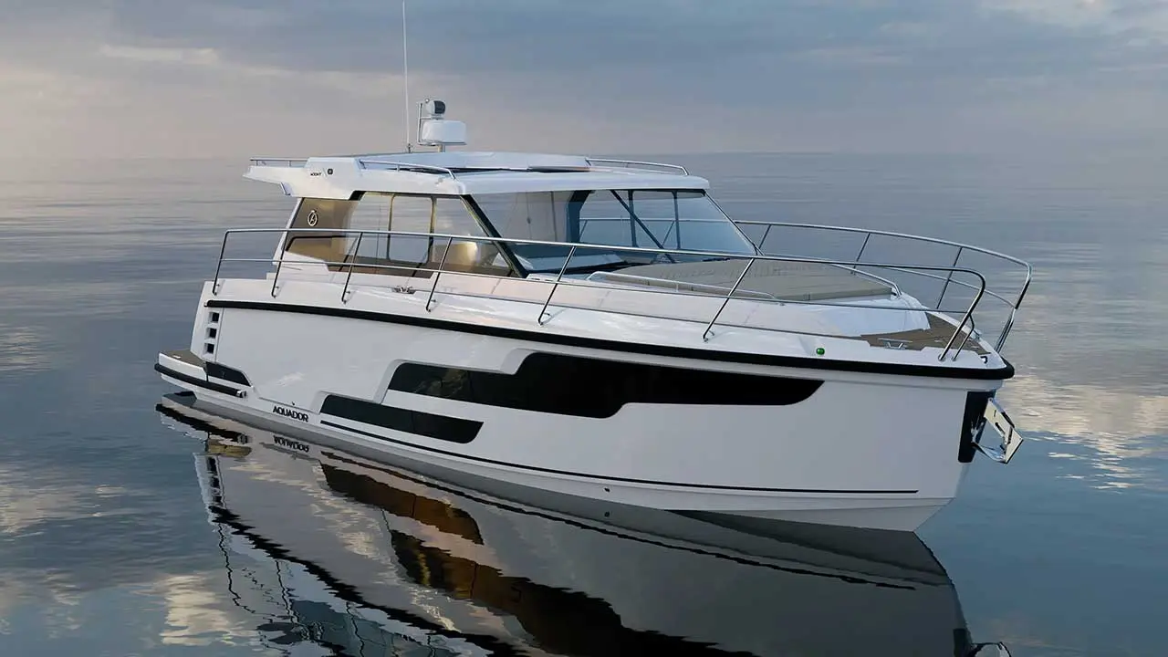 White cabin motor yacht named “AJADIOR” floating on calm sea, with its reflection visible in the water.
